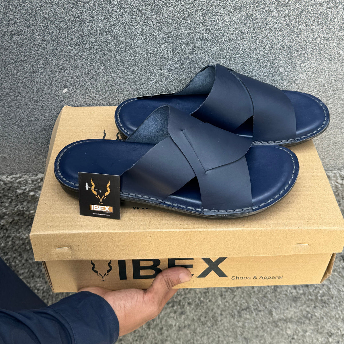 Blue sandals on a cardboard box with 'Ibex' branding, held by a hand.