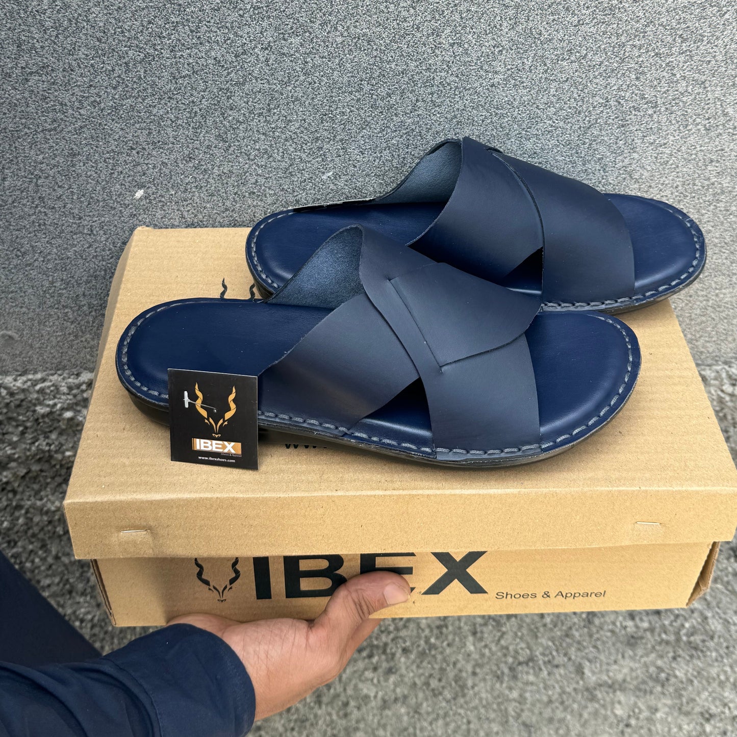 Blue sandals on a cardboard box with 'Ibex' branding, held by a hand.